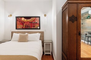 Un dormitorio con cama, mesita de noche, armario de madera y un cuadro colgado en la pared.