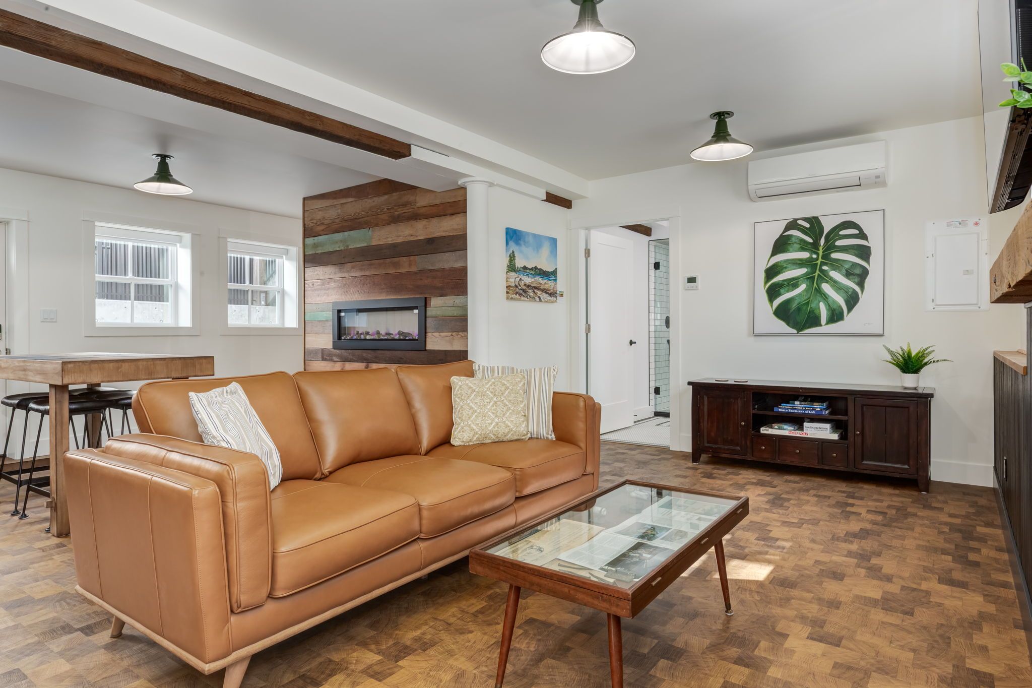 Una sala de estar moderna con un sofá de cuero, una mesa de centro de vidrio, piso de madera y un ventanal grande.