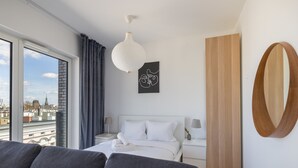 Una habitación de hotel moderna con un ventanal grande, una cama con ropa blanca, un sofá gris, una pared de acento de madera y un estilo decorativo minimalista.