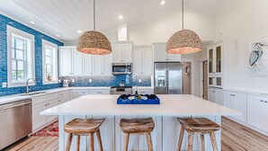 A modern kitchen with white cabinets, a large island, and wooden stools. - The Dune Buggie is an elegant, custom built 3BD/3BA home w/gulf views from every angle! (Port Saint Joe)