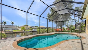 A covered swimming pool with a view of a lake and palm trees. - Gulf Access, Kayaks, Heated Pool - Villa Happy Hour - Roelens Vacations (Cape Coral)