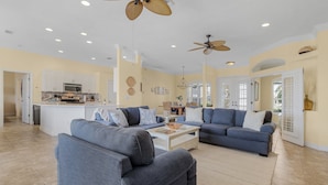 A spacious living room with two sofas, a coffee table, and ceiling fans. - Gulf Access, Kayaks, Heated Pool - Villa Happy Hour - Roelens Vacations (Cape Coral)