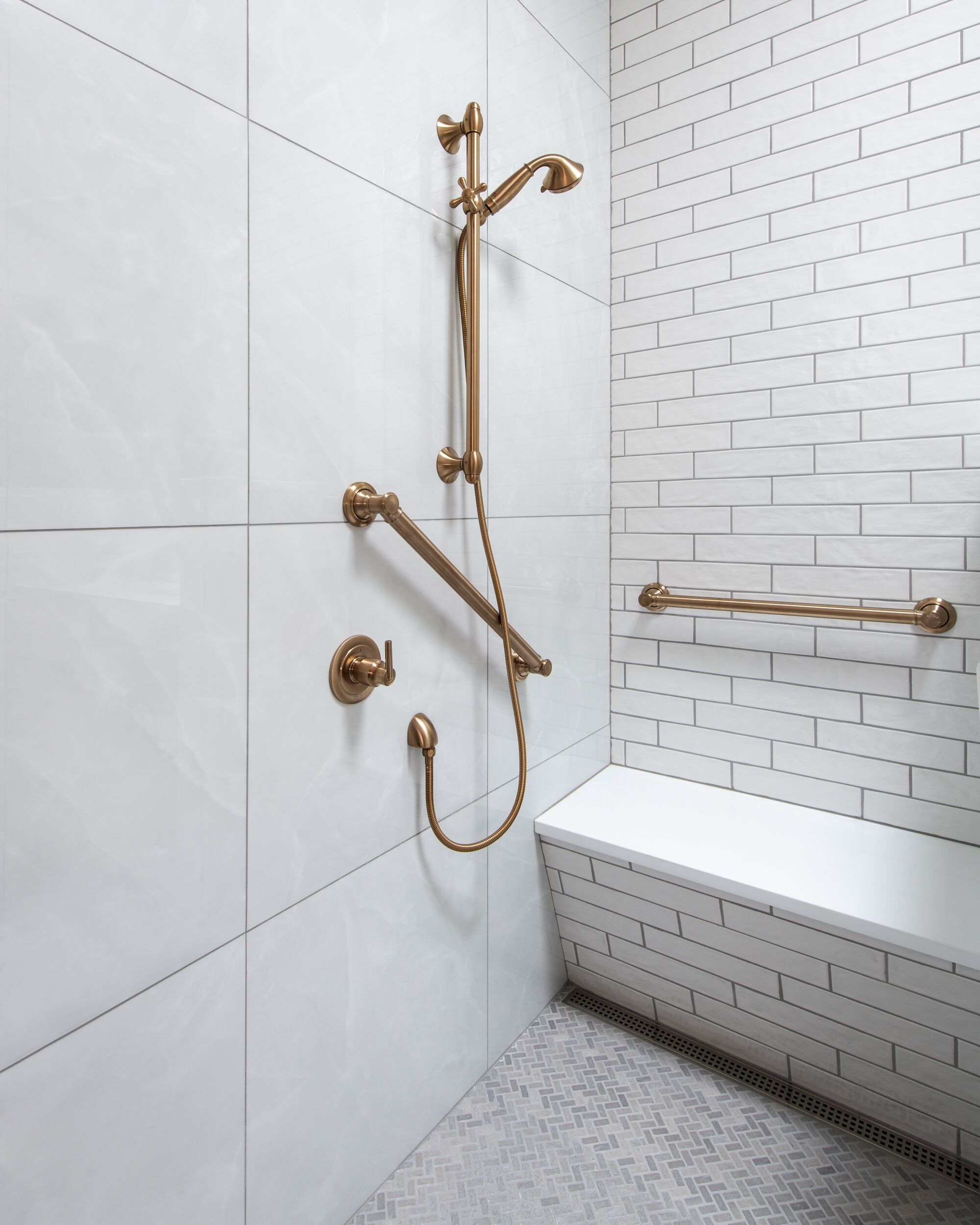 A bathroom with white tiled walls, a white bathtub, and a gold shower system.