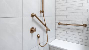 A bathroom with white tiled walls, a white bathtub, and a gold shower system.