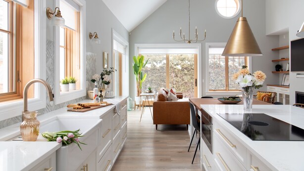 A modern kitchen with white cabinetry, a central island, and a dining area with a brown sofa. - The Haven on Halton (Perth)