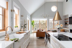 A modern kitchen with white cabinetry, a central island, and a dining area with a brown sofa.