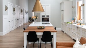 A modern kitchen with a central island, black chairs, a wooden table, and a brown leather sofa. - The Haven on Halton (Perth)