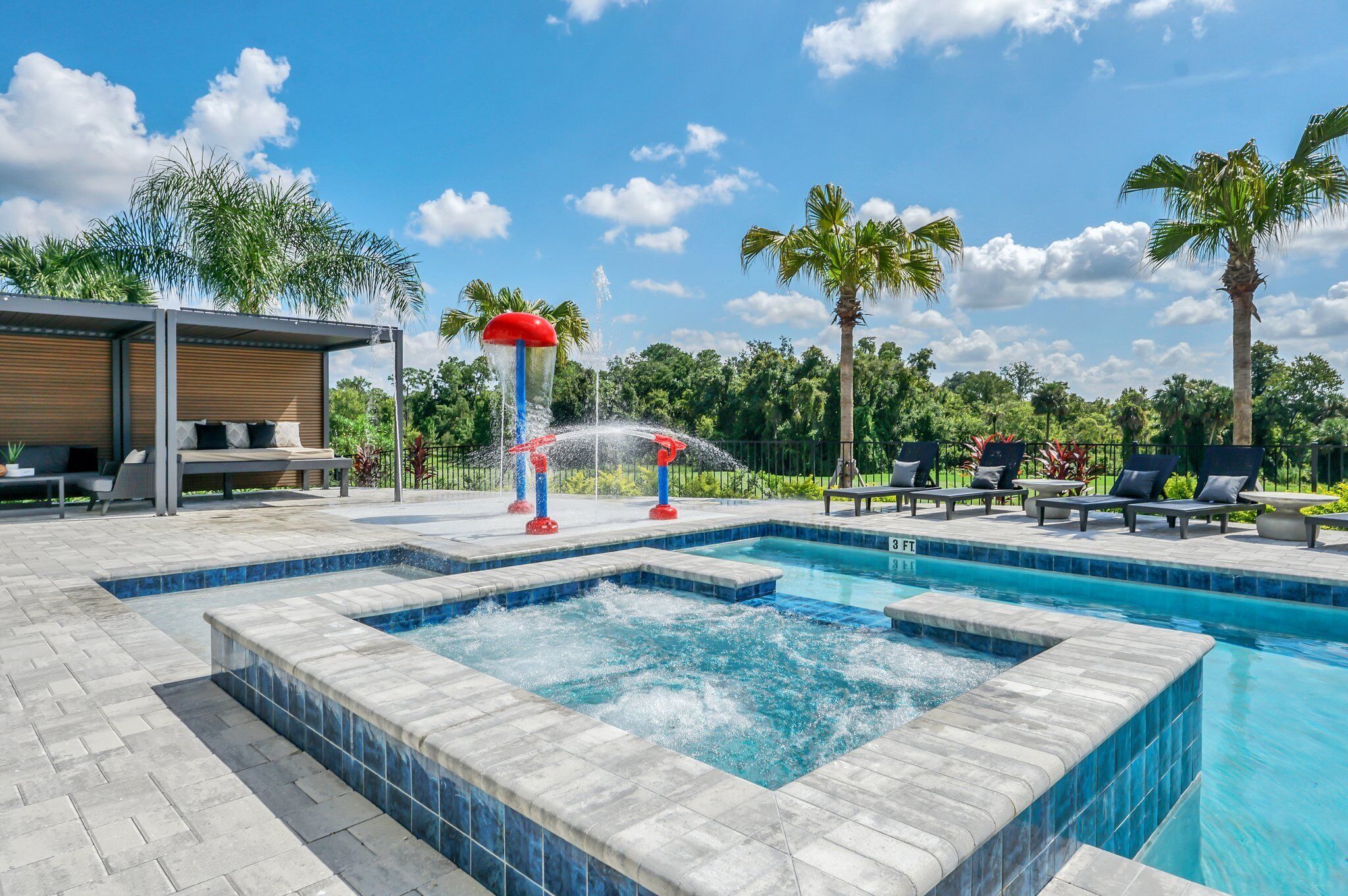 A swimming pool with a hot tub, lounge chairs, and palm trees in the background.