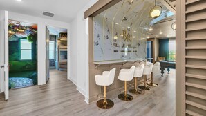 Un espace bar moderne avec un mur arrière en marbre et des touches dorées, comprenant un comptoir et des tabourets de bar blancs.