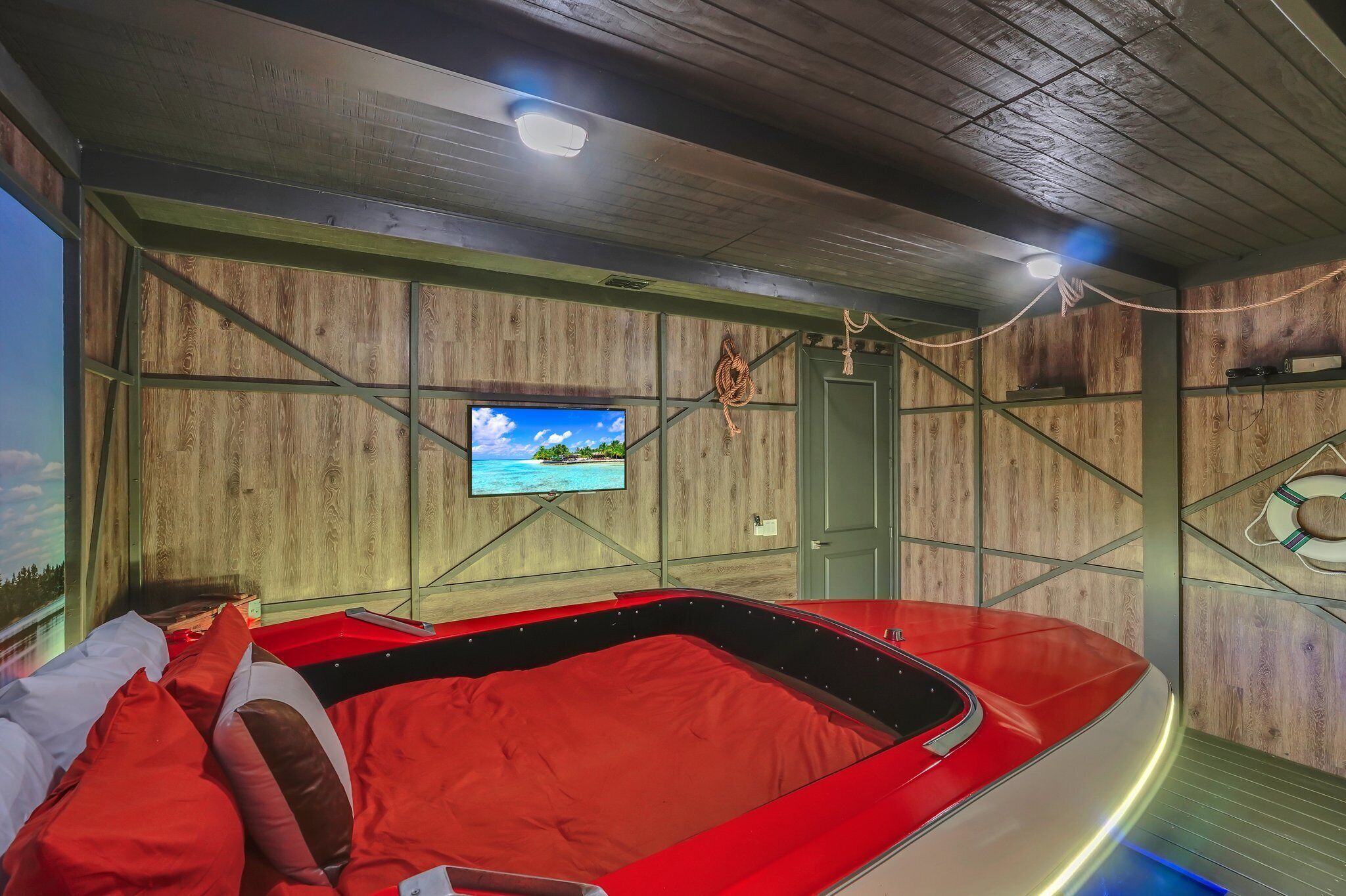 A room with a red bed, wooden walls, a television, and a door.