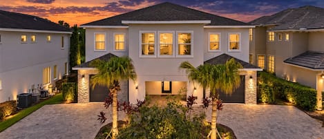 A modern two-story house with a stone facade, multiple windows, and a landscaped front yard with palm trees.