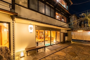 Edificio japonés tradicional con un patio de piedra, un banco de madera y un interior visible con esteras de tatami.
