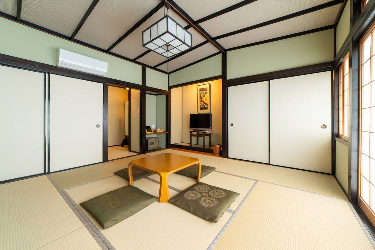 Una habitación japonesa tradicional con suelo de tatami, una mesa baja de madera, puertas correderas y un televisor.