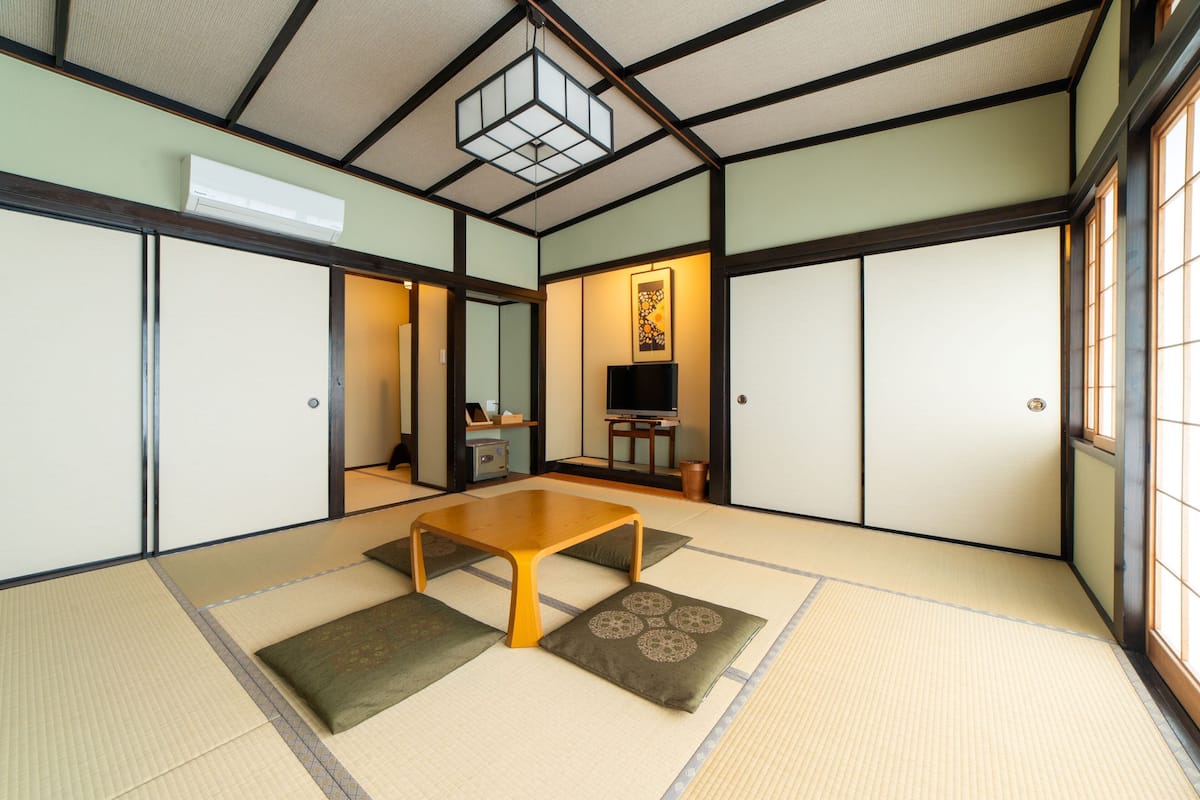 A traditional Japanese room with tatami flooring, a low wooden table, sliding doors, and a television.