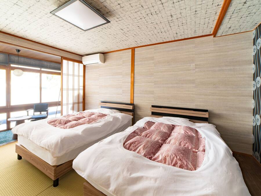 A hotel room with two beds, a sitting area with a table and chairs, and large windows.