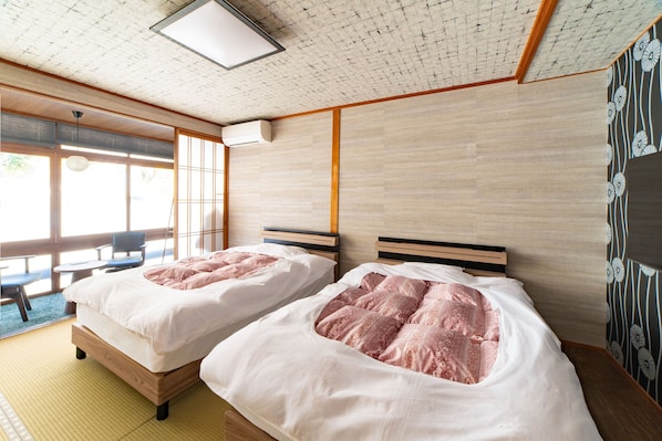 Una habitación de hotel con dos camas, un rincón de descanso con una mesa y sillas, y ventanas amplias.