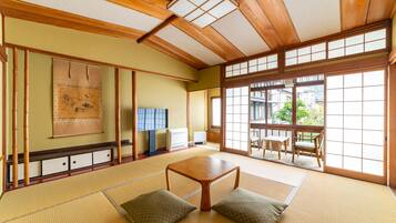 A traditional Japanese room with tatami flooring, a low wooden table, cushions, sliding doors, and a view of the outside.