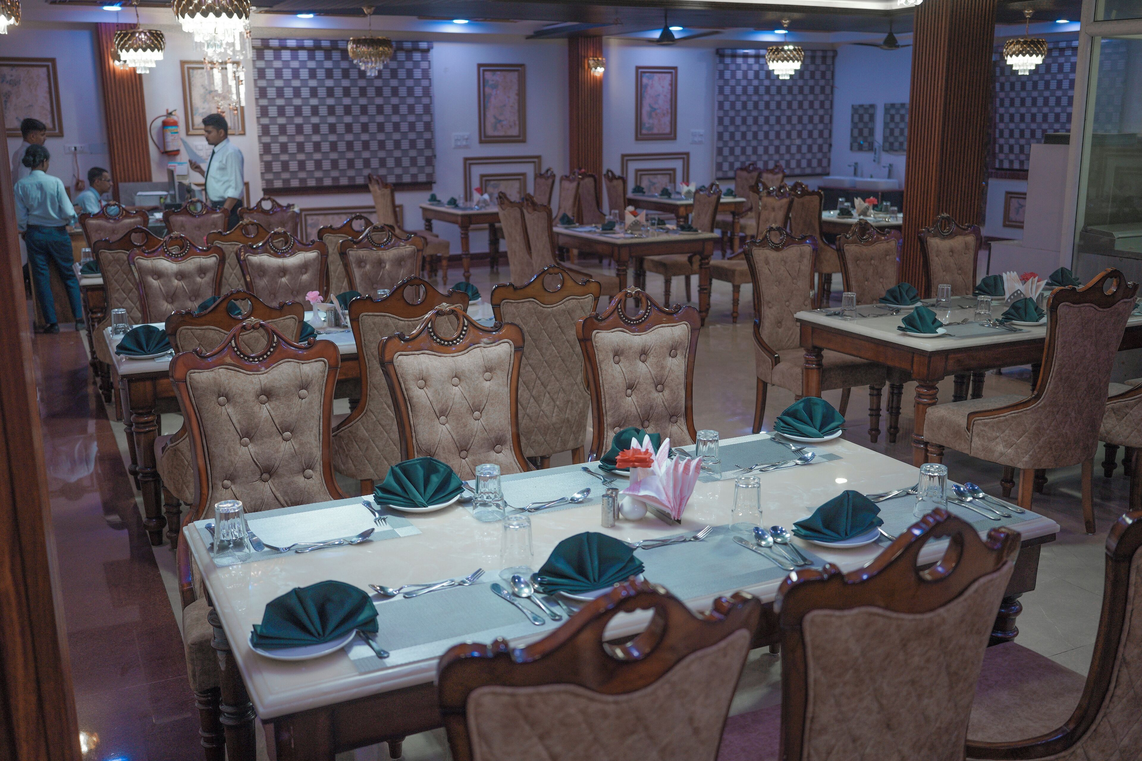 A restaurant with multiple dining tables set with green napkins, silverware, and glassware.