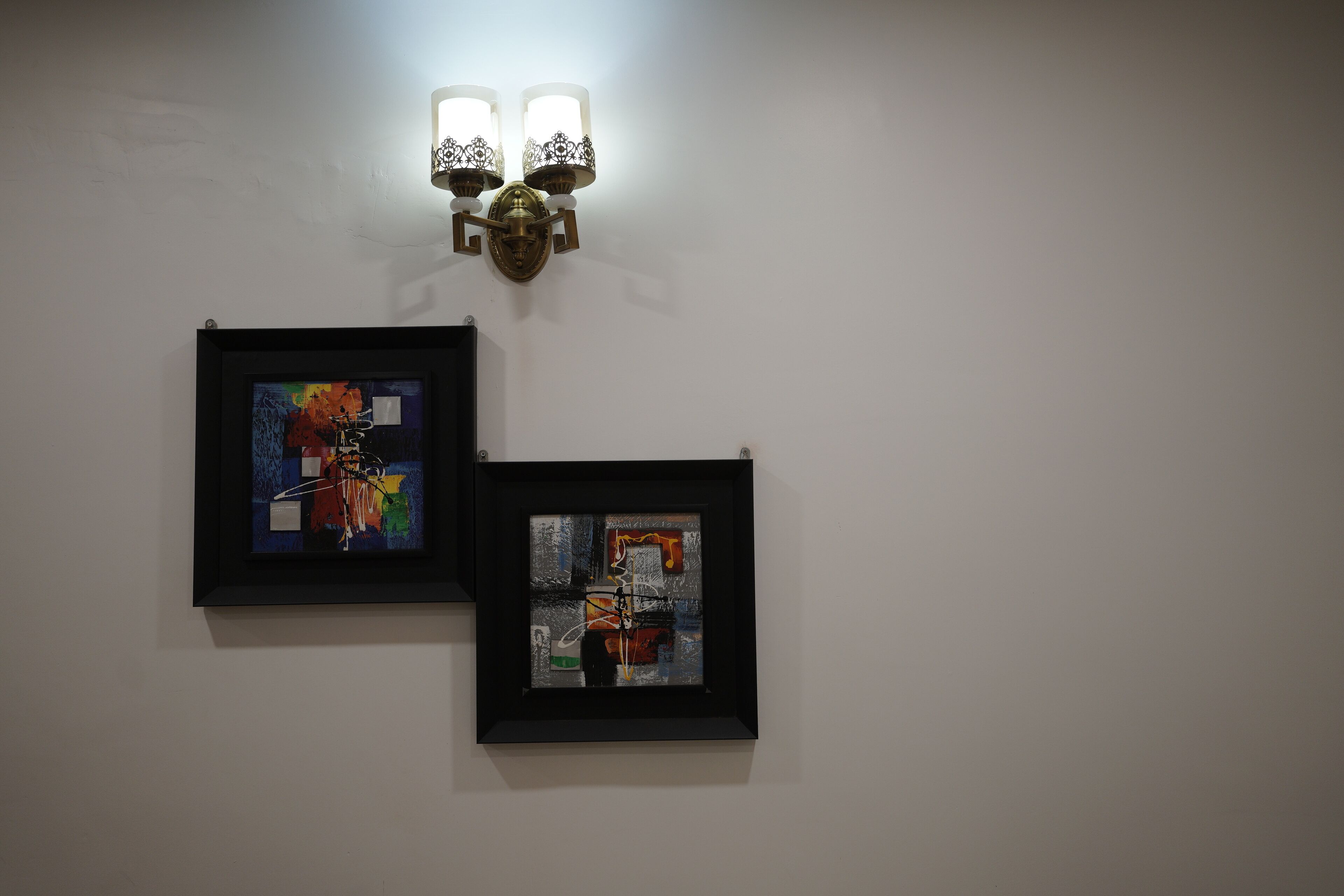 Deux tableaux abstraits encadrés sont accrochés à un mur uni, et une applique murale décorative se trouve au-dessus.