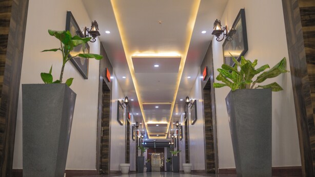 Un couloir d’hôtel moderne avec un sol réfléchissant, des plantes en pot, des appliques murales et des œuvres d’art encadrées.