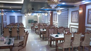 Un vaste espace dédié à la salle à manger, comprenant plusieurs tables et chaises, de magnifiques lustres et des panneaux décoratifs.