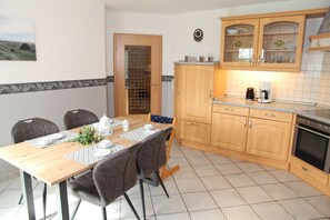 Un comedor con una mesa de madera dispuesta para cuatro, una cocina con armarios de madera y una estufa, y una puerta que da a otra habitación.