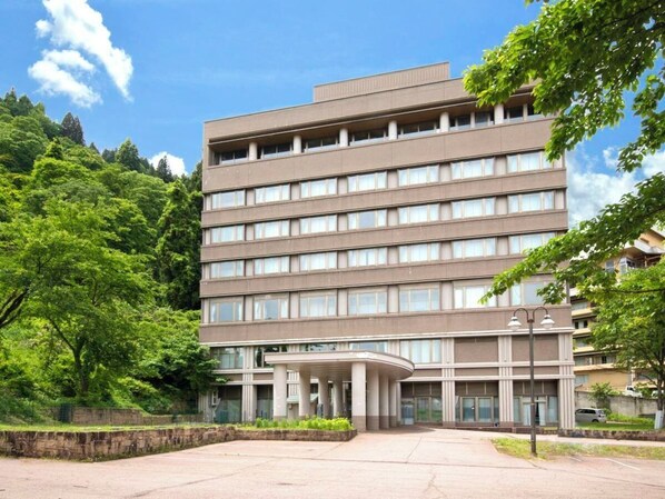 A multi-story hotel with a central entrance, surrounded by greenery and a paved driveway. - KKR Yuzawa Yukiguni (Yuzawa)