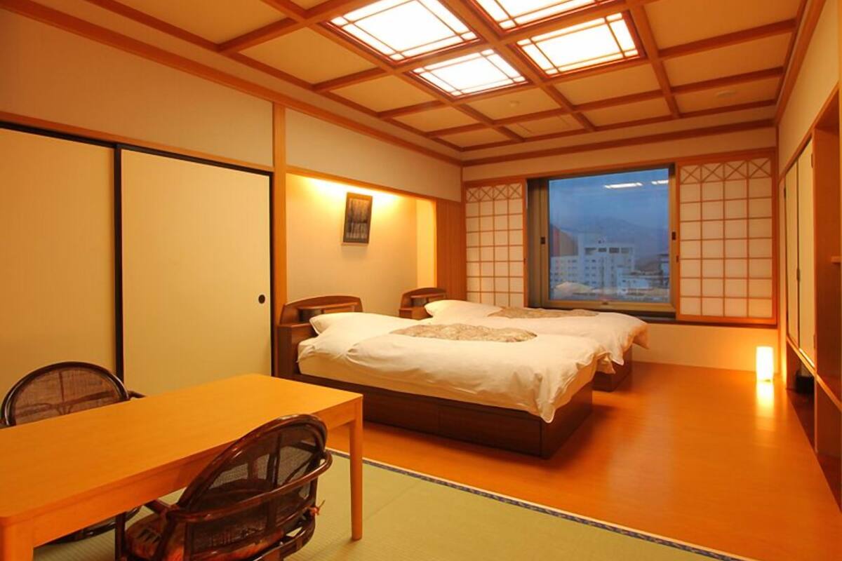 Ein traditioneller japanischer Raum mit Tatami-Böden, einem niedrigen Holzbett, einem Schreibtisch und Blick auf die Stadt.