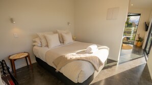 A modern bedroom with a large bed, a small wooden stool, and a view of the outdoors through a glass door. - Ben Ohau Views The Studio (Twizel)