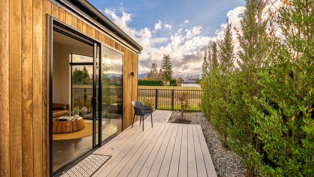 A wooden deck with a glass door leading to a room, a small outdoor seating area, and a view of a mountainous landscape. - Ben Ohau Views The Studio (Twizel)