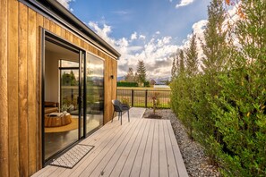 A wooden deck with a glass door leading to a room, a small outdoor seating area, and a view of a mountainous landscape. - Ben Ohau Views The Studio (Twizel)