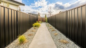 A narrow concrete pathway flanked by dark metal fences, leading to a wooden gate. - Ben Ohau Views The Studio (Twizel)