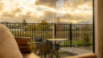 A balcony with a table and chairs, a view of a mountainous landscape, and a fence.