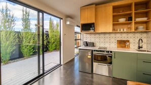 A modern kitchen with a large sliding glass door leading to a deck, stainless steel appliances, and wooden cabinets. - Ben Ohau Views The Studio (Twizel)