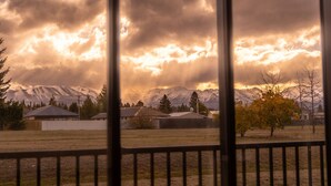 Vista a través de una ventana que muestra una zona residencial con casas, un árbol y montañas al fondo.