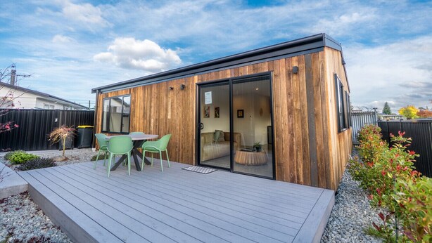 Una cabaña moderna de madera con terraza, puertas corredizas de vidrio y una pequeña zona de estar al aire libre.
