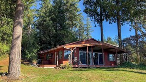 Eine Hütte mit einer großen Veranda, einem überdachten Sitzbereich im Freien und Blick auf den umliegenden Wald.