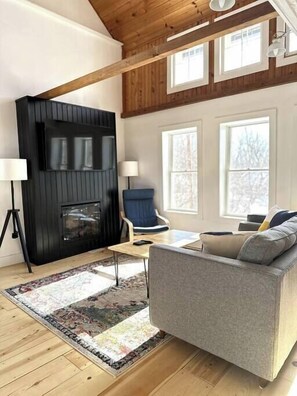 A modern living room with a black fireplace, a grey sofa, a blue chair, and a patterned rug.