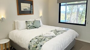 A neatly made bed with white linens and floral-patterned blankets, a framed picture on the wall, and a window with a view of trees. - Springdale Gums: Denmark Forest Retreat (Hay)