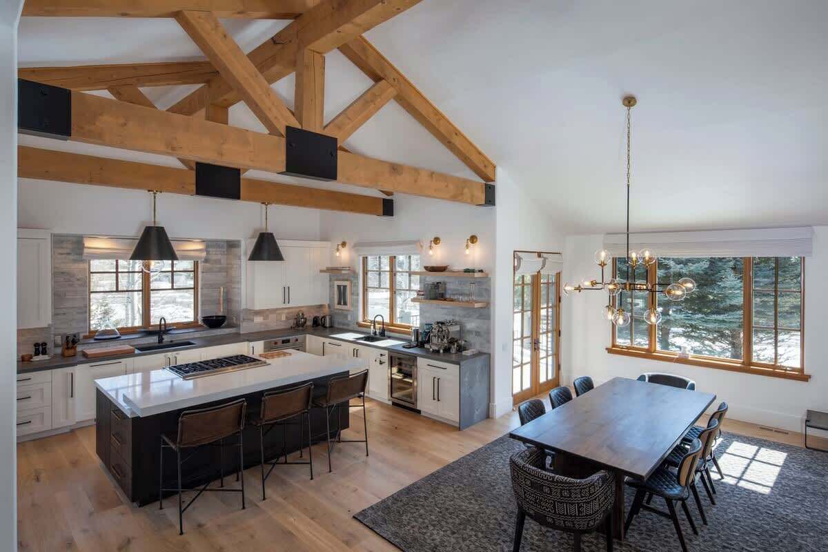 Een ruime keuken met een groot kookeiland, houten balken, hanglampen en een eethoek met uitzicht.