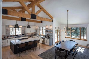 Una cocina amplia con una isla grande, vigas de madera, lámparas colgantes y un comedor con vistas.