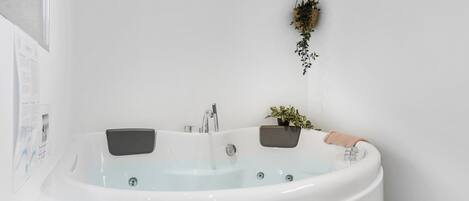 Une salle de bain moderne avec une baignoire sur pieds, deux vasques fixées au mur et une petite plante en pot.