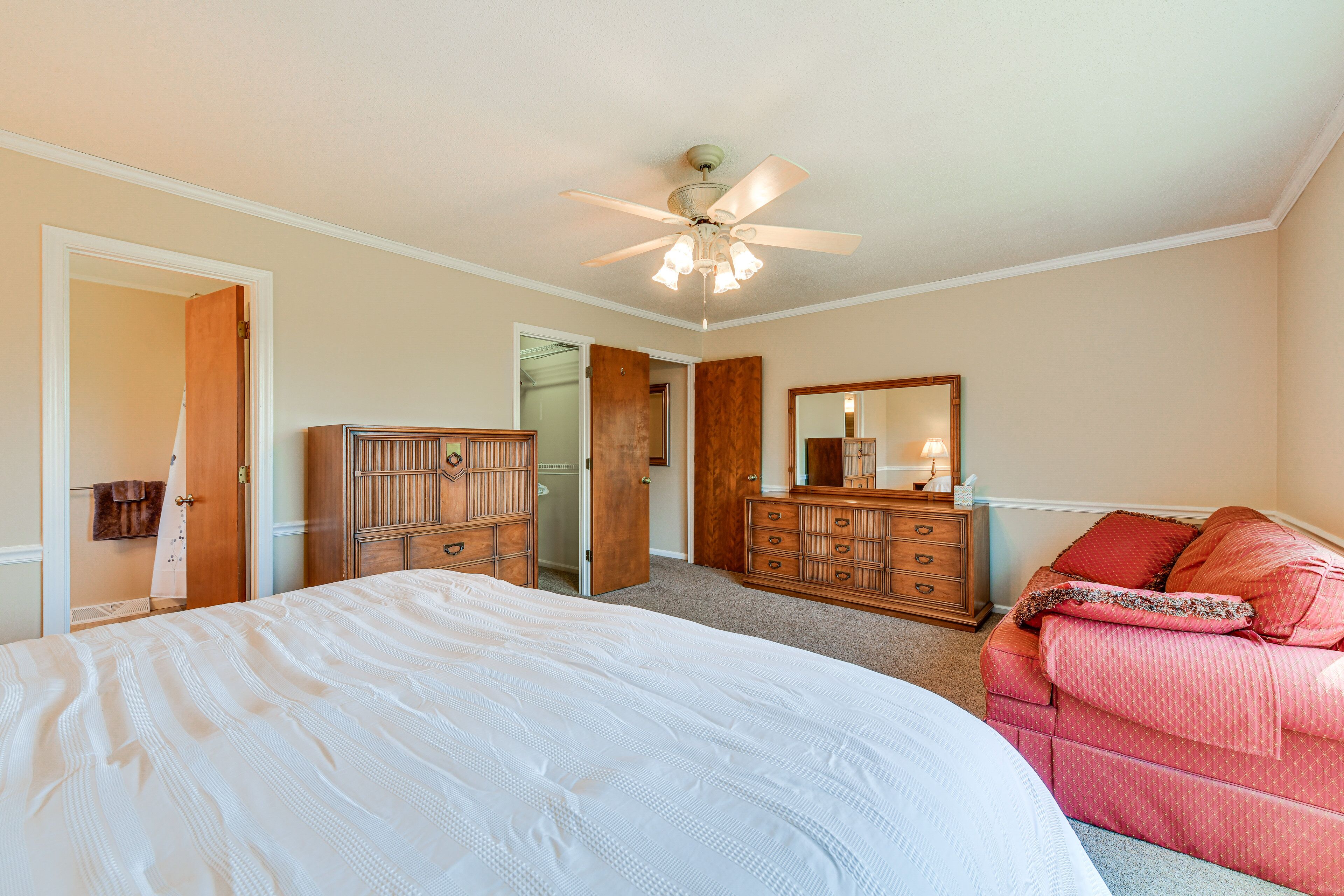 Quarto com cama grande, cômoda de madeira, toucador com espelho e ventilador de teto.