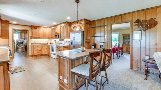 A spacious kitchen with wooden cabinets, a central island, and a dining area with chairs. - Spacious Mount Pleasant Home w/ Grill & Yard! (Mt Pleasant)