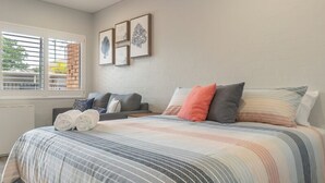 A bedroom with a bed, pillows, a sofa, and a window with blinds. - Coasters 18 - steps from downtown Sawtell (Sawtell)