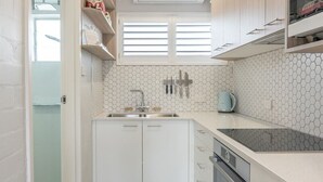 A compact kitchen with white cabinets, a black stove, a sink, and a window with blinds. - Coasters 18 - steps from downtown Sawtell (Sawtell)