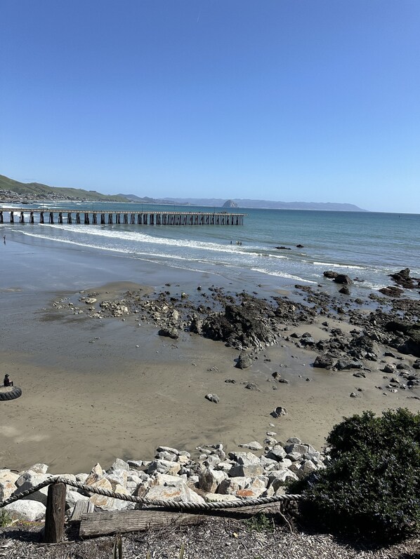 A beach with a rocky shoreline, a wooden pier extending into the water, and distant hills.