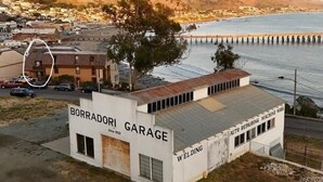 A white building labeled "BORRADORI GARAGE" with "WELDING" and "AUTO REPAIR MACHINE WORK" signs. - Oceanfront condo with PRIVATE deck. Pet friendly. Just a short walk to town. (Cayucos)