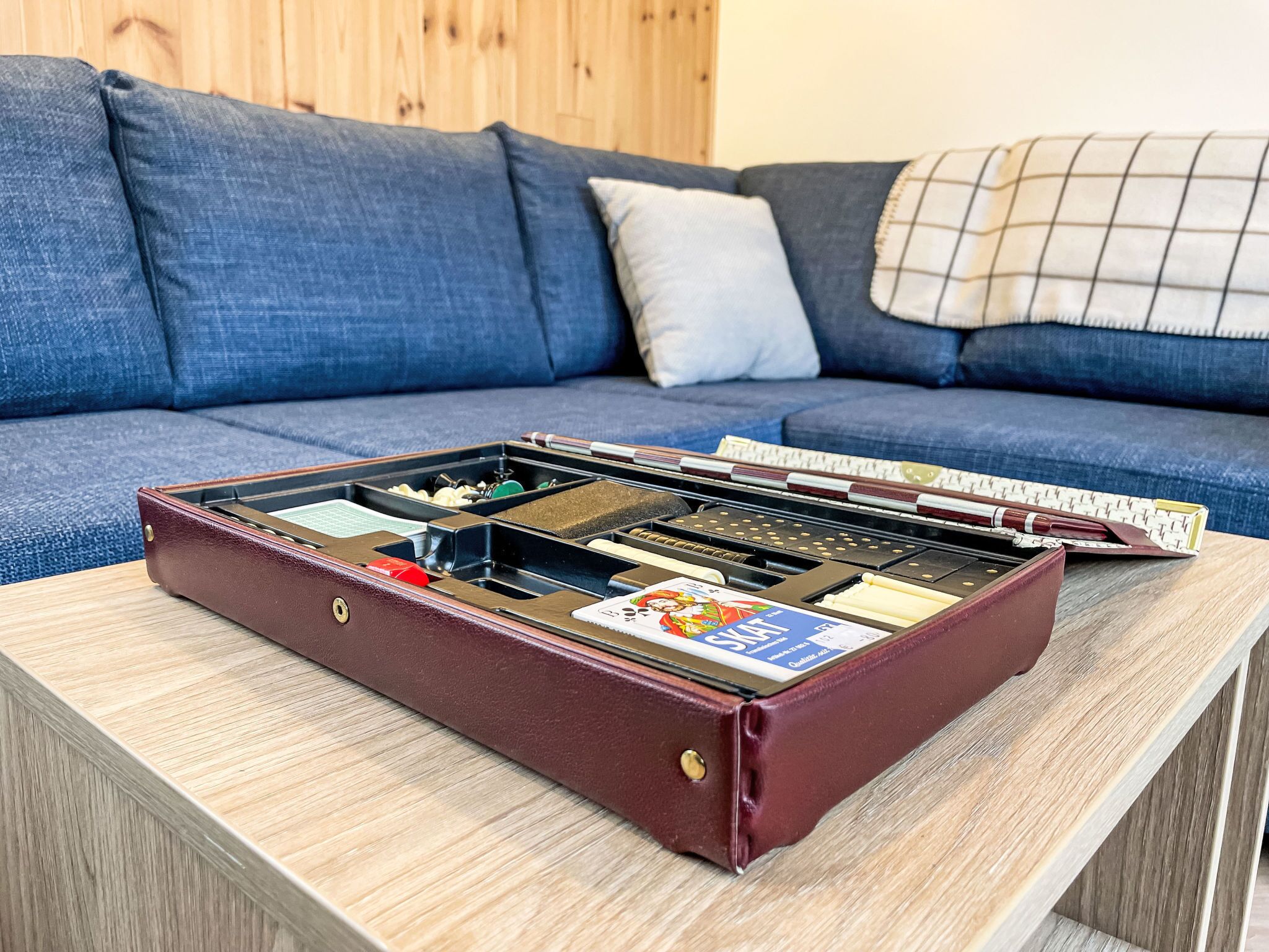 A suitcase with compartments on a wooden table in a room with a blue sofa and a wooden wall.