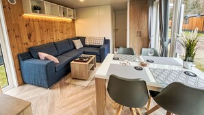 A modern living room with a blue sofa, a wooden coffee table, and a dining area with a white table and chairs. - Tiny Haus Christas Angler-Oase by Interhome (Riedenburg)